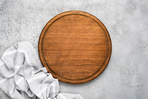 Round wooden cutting board and linen textile on grey concrete background with copy space for text. Food background