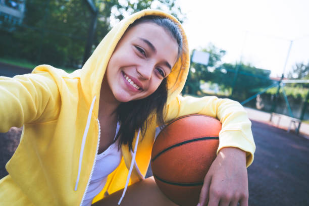 Teenage girl practicing basketball and making selfie Teenage girl practicing basketball and making selfie at basketball court. selfie girl stock pictures, royalty-free photos & images