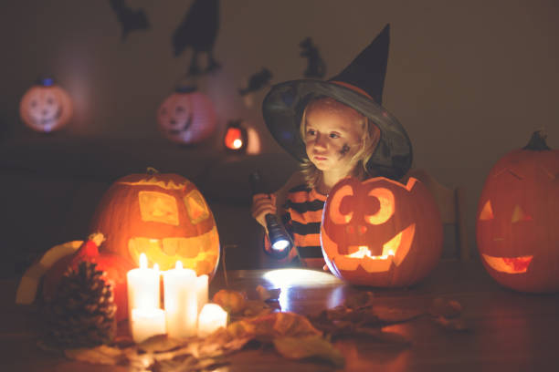 Adorable child, toddler girl, playing with Halloween carved pumpkin and decoration Adorable child, toddler girl, playing with Halloween carved pumpkin and decoration at home halloween pumpkin human face candlelight stock pictures, royalty-free photos & images