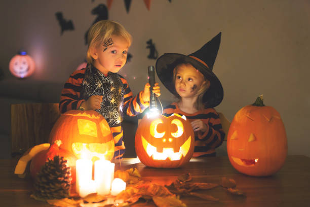 Adorable children, toddler boy and girl, playing with Halloween carved pumpkin and decoration at home Adorable children, toddler boy and girl, playing with Halloween carved pumpkin and decoration at home halloween pumpkin human face candlelight stock pictures, royalty-free photos & images