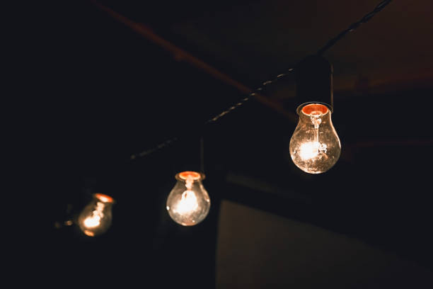 istock Old-fashioned luminous bulbs hanging on a wire in a dark room 1182521540