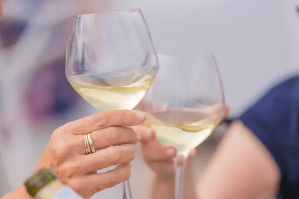 Photo of Photo detail of two hands together holding two glasses of white wine. Concept of celebration.