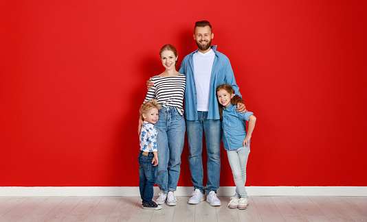 happy family mother father and children daughter and son  near an empty red wall