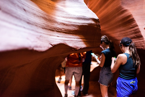 Page, USA - August 10, 2019: Tour group of young people walking on trail inside Upper Antelope slot canyon in Arizona and abstract sandstone formations