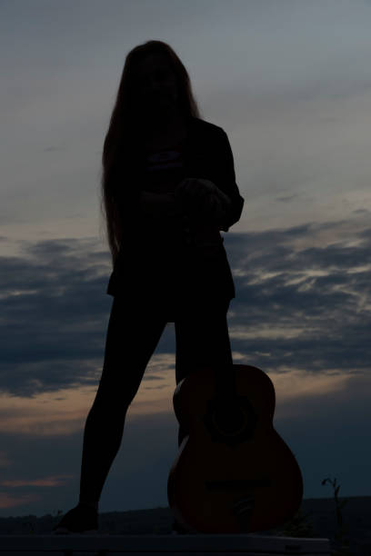 istock Silhouette woman playing guitar in sunset 1182527663