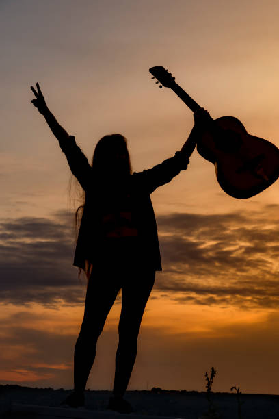 istock Silhouette woman playing guitar in sunset 1182527671