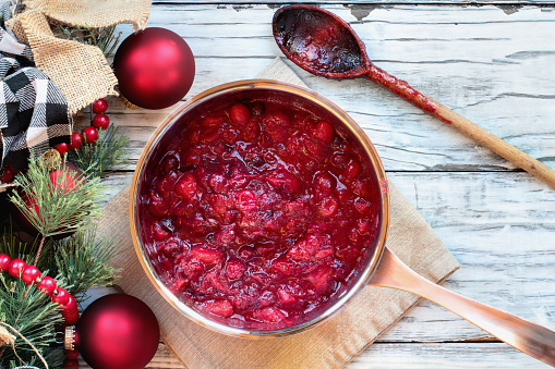 Sauce pan of cranberry relsih over a white wood table background with messy wooden spoon and Christmas decorations. Top view.