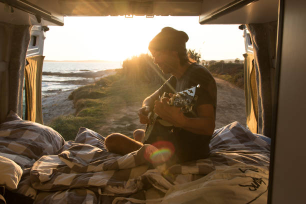 istock Man playing guitar in the van at sunset 1182533881