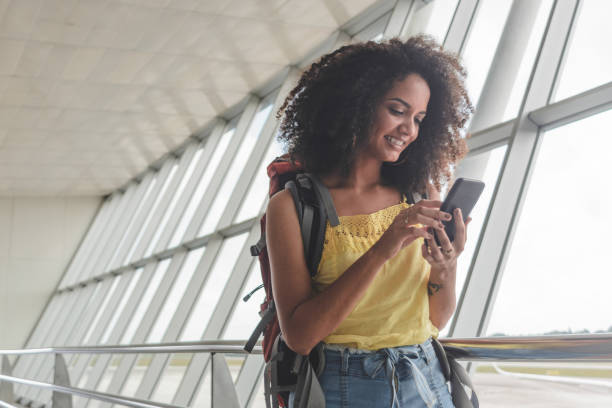 空港で彼女の搭乗スケジュールをチェックバックパックを持つ若い女性 - airport passengers ストックフォトと画像