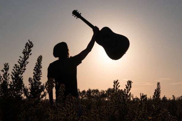 istock Man holding a guitar against the evening sky 1182534936