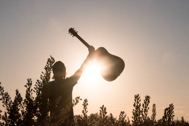 istock Man holding a guitar against the sun 1182534998
