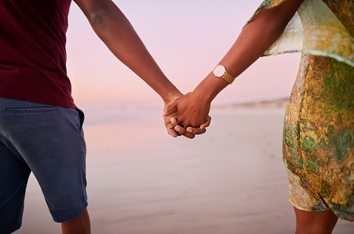 Close-up shot of a african couple holding hands walking together on a beach