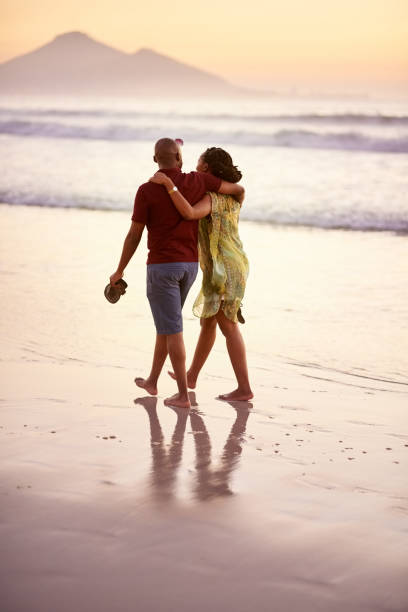 There's something romantic about the beach Rear view shot of loving young couple walking together along the sea shore black couple sunset stock pictures, royalty-free photos & images