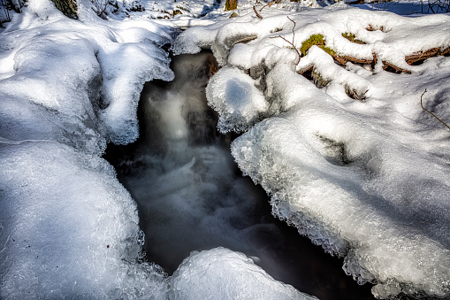 Winter wonderland with river and icy surrounding framed by a flowing creek, long exposure that bring forward a creature looking shape in water