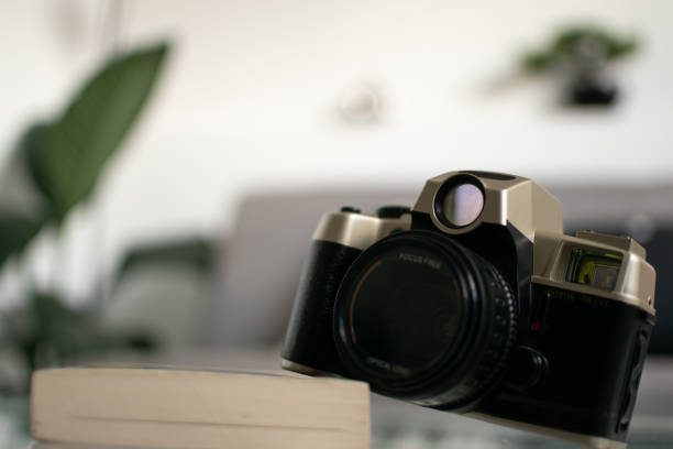 istock Black and brown analog camera standing on a book with bokeh and plants on the background 1182537656