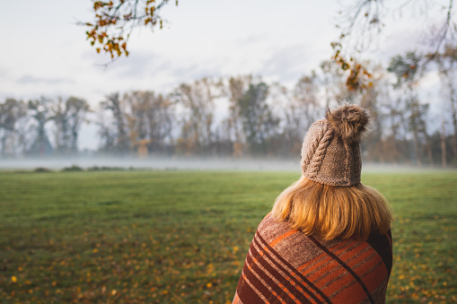 Woman with blanket and knit hat enjoying cold misty morning outdoors.