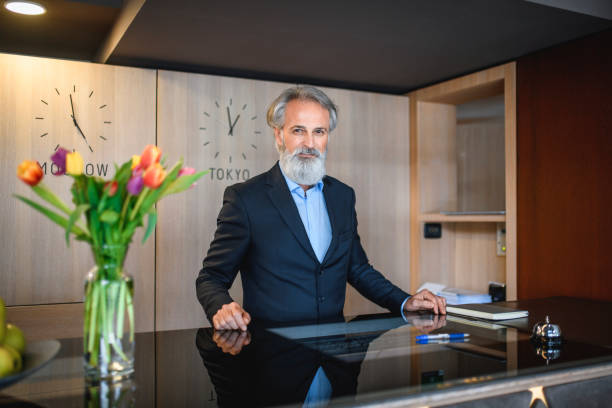 istock Welcoming Senior Hotel Receptionist Standing at Front Desk 1182549213
