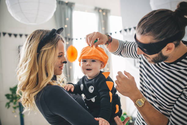 Family at Halloween home party Group of Young people at home celebrating Halloween in costumes, baby of one couple is joined the party carnival mask women party stock pictures, royalty-free photos & images