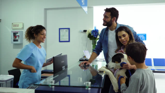 Happy Latin American family taking their dog to the vet and friendly receptionist giving a treat to the dog
