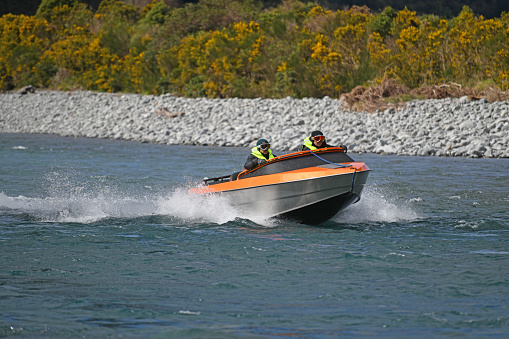 Taramakau River, West Coast, New Zealand, August 29, 2019:  Two people power their jetboat down the Taramakau River on the West Coast of New Zealand.