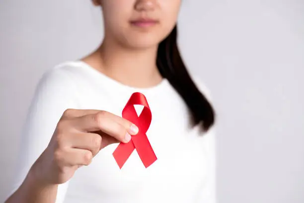 Photo of Closeup woman hand holding red ribbon HIV, world AIDS day awareness ribbon. Healthcare and medicine concept.