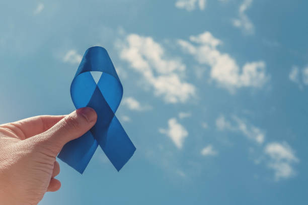 Hand holding blue ribbon on blue sky background , Prostate Cancer Awareness, Men health awareness, November blue, International Men's Day, world diabetes day stock photo