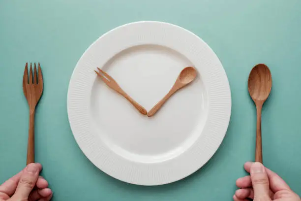 wooden spoon and fork as a clock hands on white plate, Intermittent fasting concept, ketogenic diet, weight loss, skip meal