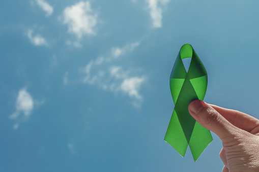 mano sosteniendo la cinta verde sobre el cielo azul, conciencia ción sobre la salud mental y concienciación sobre el linfoma, Día Mundial de la Salud Mental photo