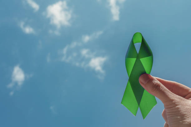 hand holding Green Ribbon over blue sky, Mental health awareness and Lymphoma Awareness, World Mental Health Day hand holding Green Ribbon over blue sky, Mental health awareness and Lymphoma Awareness, World Mental Health Day lymphoma photos stock pictures, royalty-free photos & images