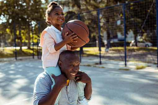 Close up of a grandfather taking his granddaughter to play some basketball in the park