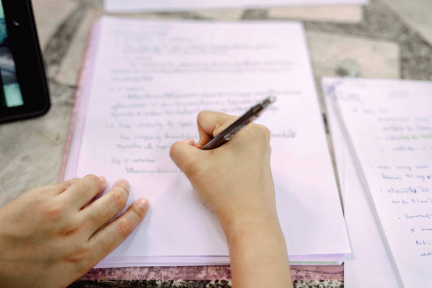 Close up photo of adult male writing note in white paper. Focus on the hands holding a pen and a white note. The background is white. Its in indoor restaurant in the afternoon.