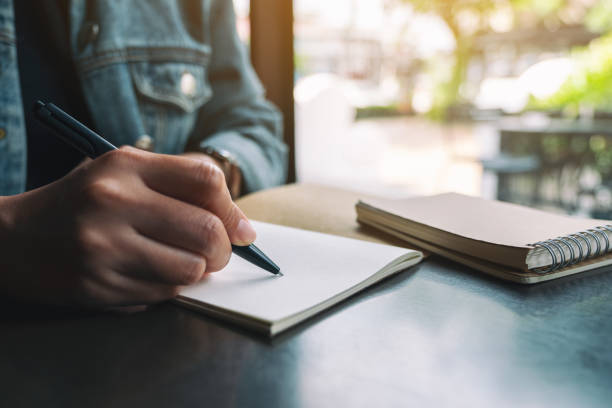 istock a woman writing on a blank notebook on wooden table 1182576287