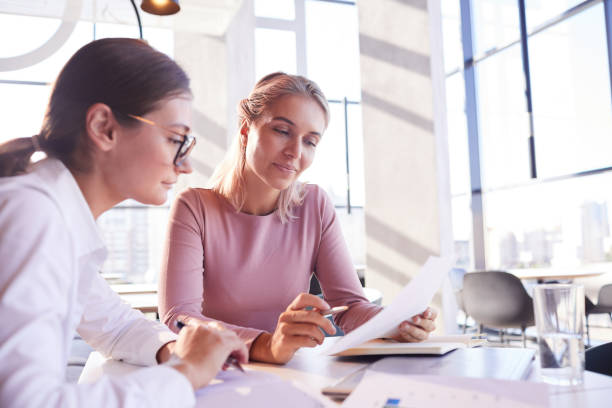 istock Content pensive young attractive ladies sitting at table in cafe and viewing data while brainstorming about brining product to market 1182584996