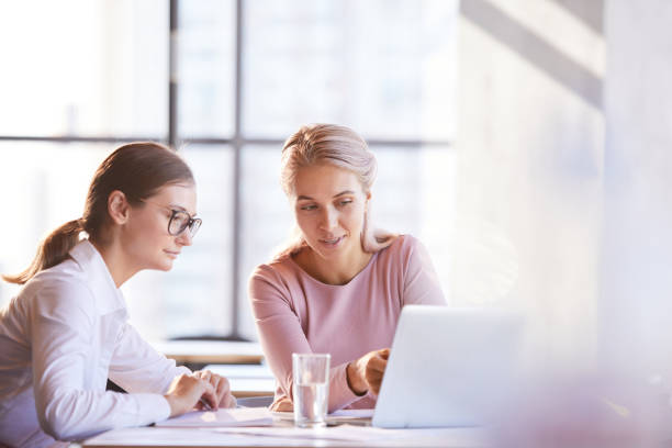 istock Content thoughtful young ladies sitting at table in cafe and using laptop while discussing web project 1182585031