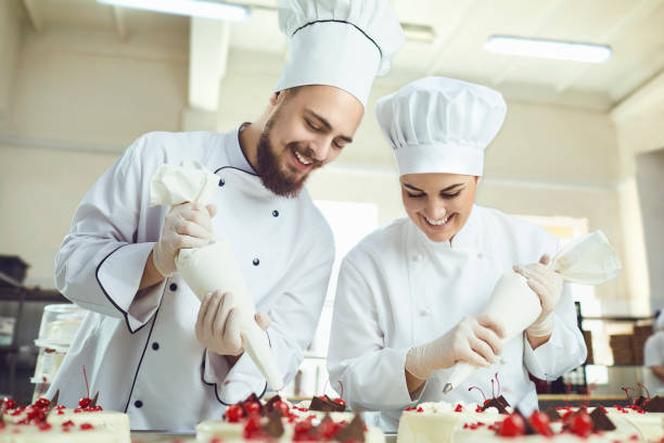 Confectioners with a bag for the cream will decorate the cake in the pastry shop.