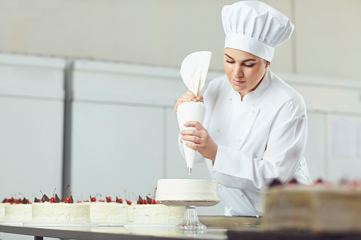 Confectioner woman decorating cake in pastry shop.
