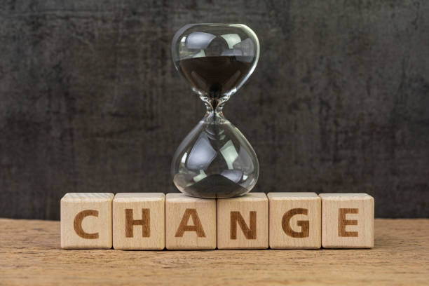 istock Change, transform or evolve concept, sand glass or hourglass on cube block with alphabet building the word Change on wood table with dark black background 1182586218