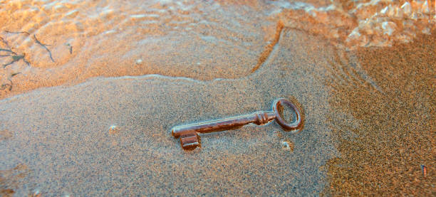 la grande chiave di ferro per lo scrigno del tesoro lavato sulla spiaggia sabbiosa - skeleton key foto e immagini stock