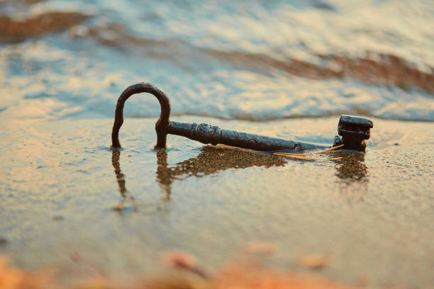 una vecchia chiave del tesoro arrugginito perso, sdraiato nella sabbia nel surf sulla spiaggia. il concetto di fortuna e ricchezza inaspettata - skeleton key foto e immagini stock