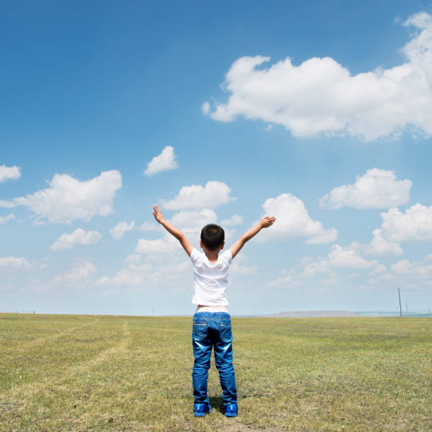 istock Little boy arms raised under blue sky 1182594093