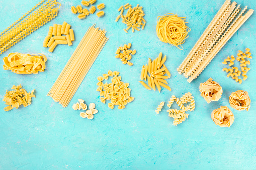 Italian pasta variety, flat lay banner, shot from the top on a blue background with a place for text