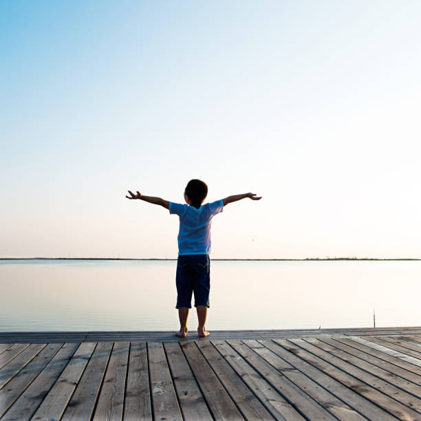 istock Little boy standing at lakeside with arms outstretched 1182600615