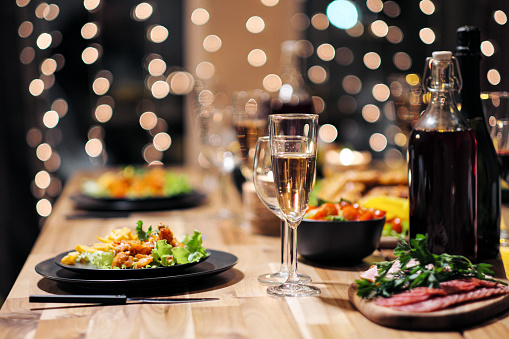 Festive table setting. Food and drinks, plates and glasses. Evening lights and candles. New Year's Eve Christmas Dinner.