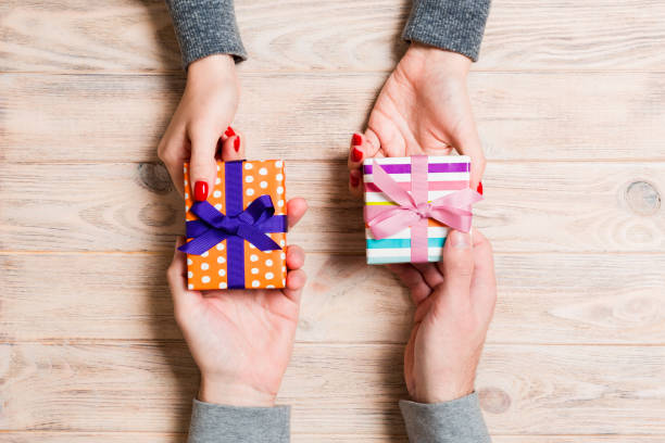 나무 배경에 선물을 교환 하는 여자와 남자의 상단 보기. 부부는 서로에게 선물을 준다. 휴일 개념에 대한 놀라움을 만드는 클로즈업 - gift ribbon straight wrapped 뉴스 사진 이미지