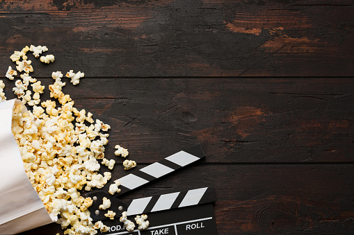 Cinema concept. Popcorn in a box and movie clapper on wooden background top view. Free space