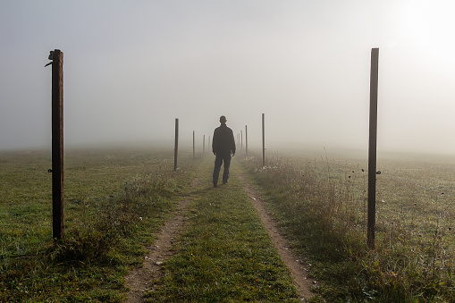 Young man walk on path with wooden stick in misty fog at sunrise, Czech landscape