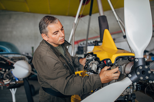 One man, airplane mechanic and pilot repairing propeller airplane in airplane hangar.