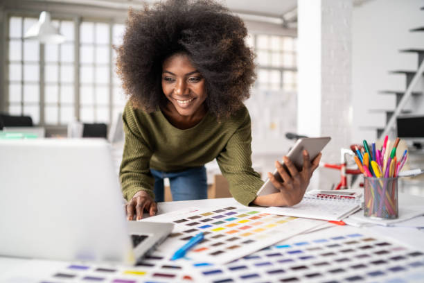 African Fashion designer working in studio and using laptop and smart phone Fashion designer working in studio. Young black woman in an office smiling to camera, close up product designer photos stock pictures, royalty-free photos & images