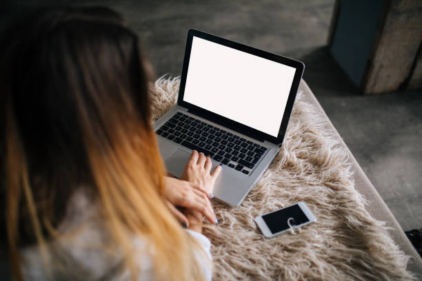 Woman using blank screen laptop on bed