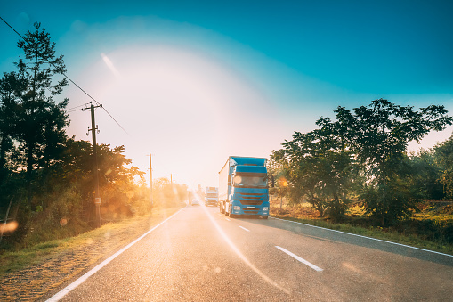 Truck In Motion On Country Road In Sunset Sun Sunshine Natural Sunlight. Tractor Unit, Prime Mover, Traction Unit On Countryside Road In Europe. Business Transportation And Trucking Industry Concept